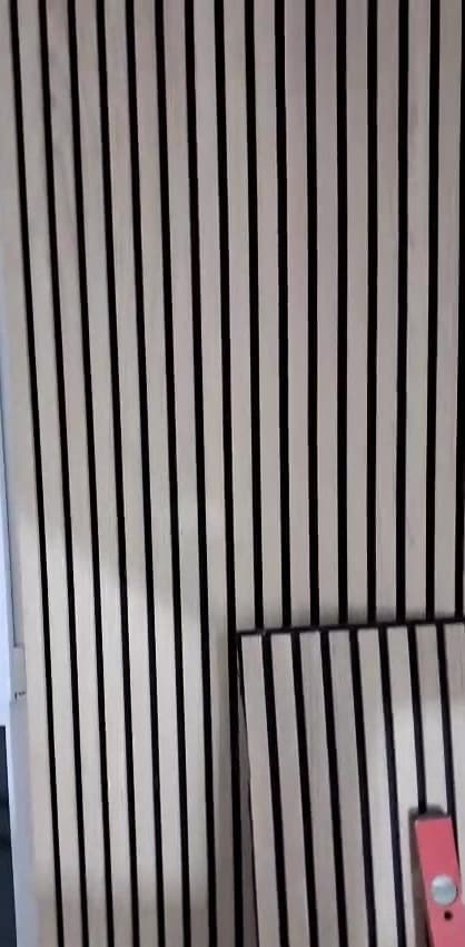 Nahaufnahme senkrechter Holzlamellen mit dunklen Zwischenräumen, davor lehnt ein weiteres Lamellenpaneel, unten rechts ein Werkzeug